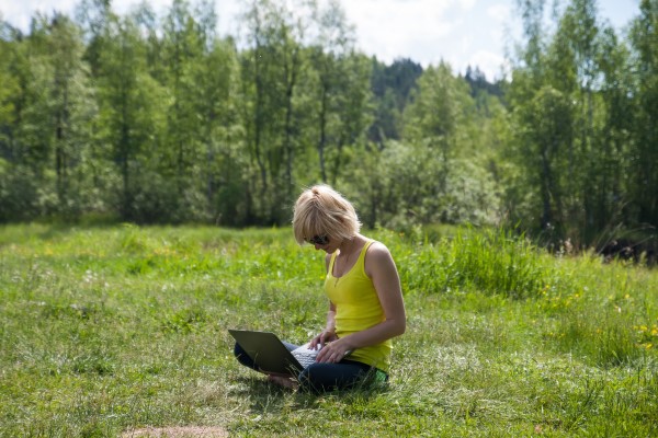 Девушка работает за ноутбуком и сидит на траве